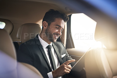 Buy stock photo Cropped shot of a handsome young businessman using a tablet while on his morning commute to work