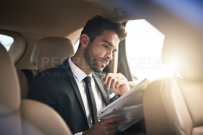 Buy stock photo Cropped shot of a handsome young businessman reading the paper while on his morning commute to work