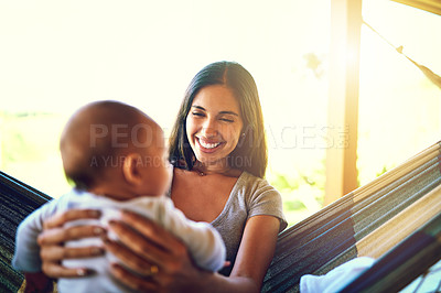 Buy stock photo Shot of a cheerful young mother holding her baby infant son while smiling at him outside at home