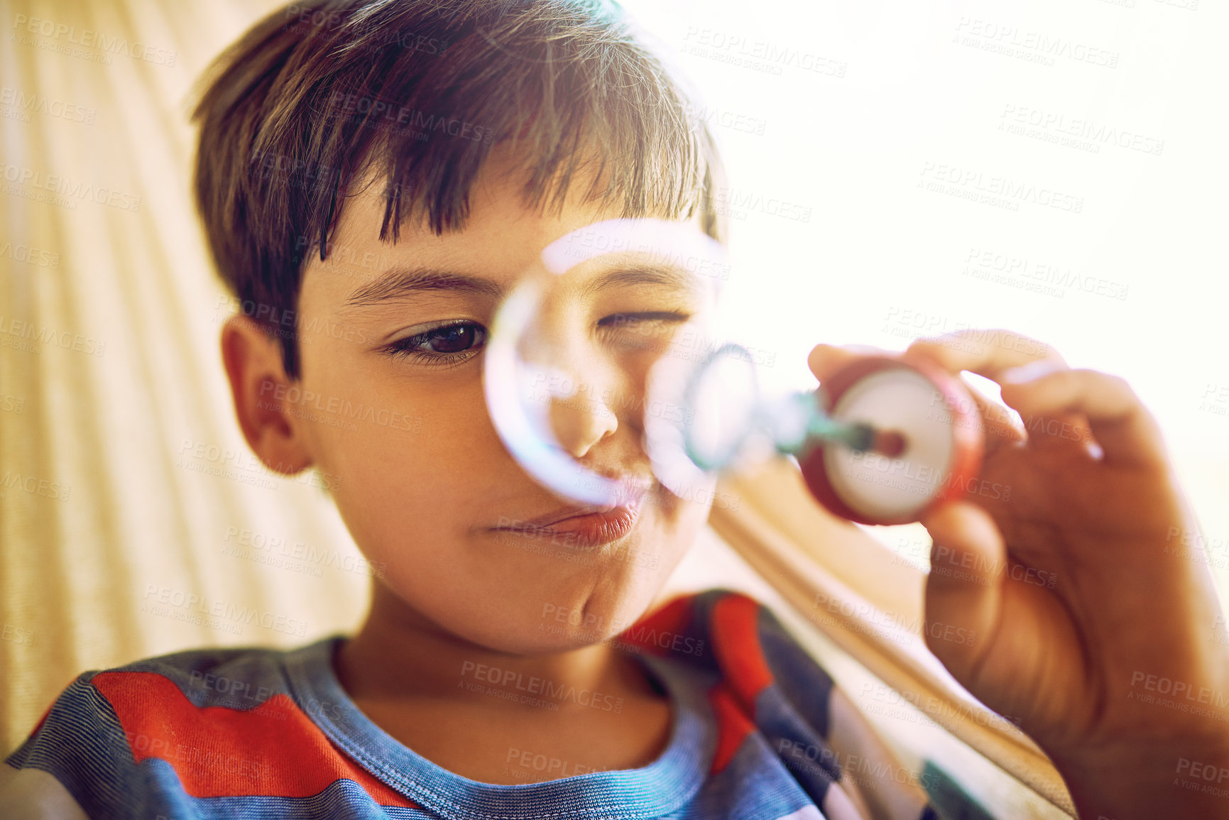 Buy stock photo Shot of a curious little boy holding up and looking through a bubble he just blew outside during the day