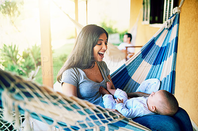 Buy stock photo Shot of a cheerful young mother relaxing on a hammock with her infant son outside at home during the day