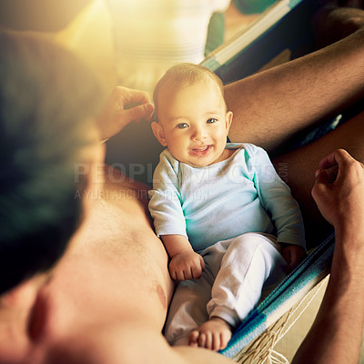 Buy stock photo Portrait of a cheerful baby boy seated on his fathers lap while looking at the camera outside at home during the day