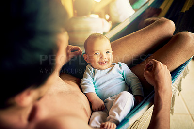 Buy stock photo Portrait of a cheerful baby boy seated on his fathers lap while looking at the camera outside at home during the day