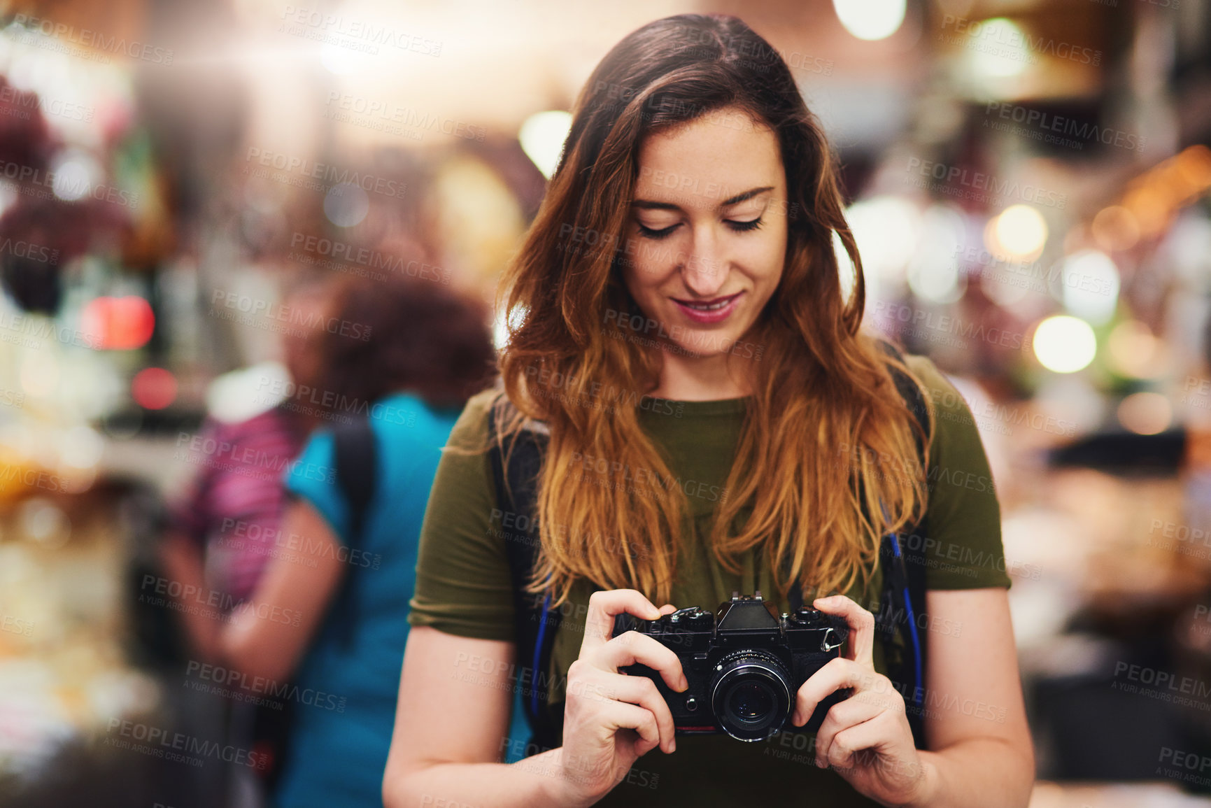 Buy stock photo Shot of a cheerful young woman holding a camera and looking on the screen while standing at a market outside during the day