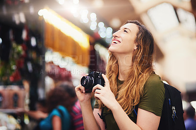 Buy stock photo Shot of a cheerful young woman taking photos of market stalls at a busy bazaar outside during the day