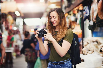 Buy stock photo Shot of a cheerful young woman taking photos of market stalls at a busy bazaar outside during the day