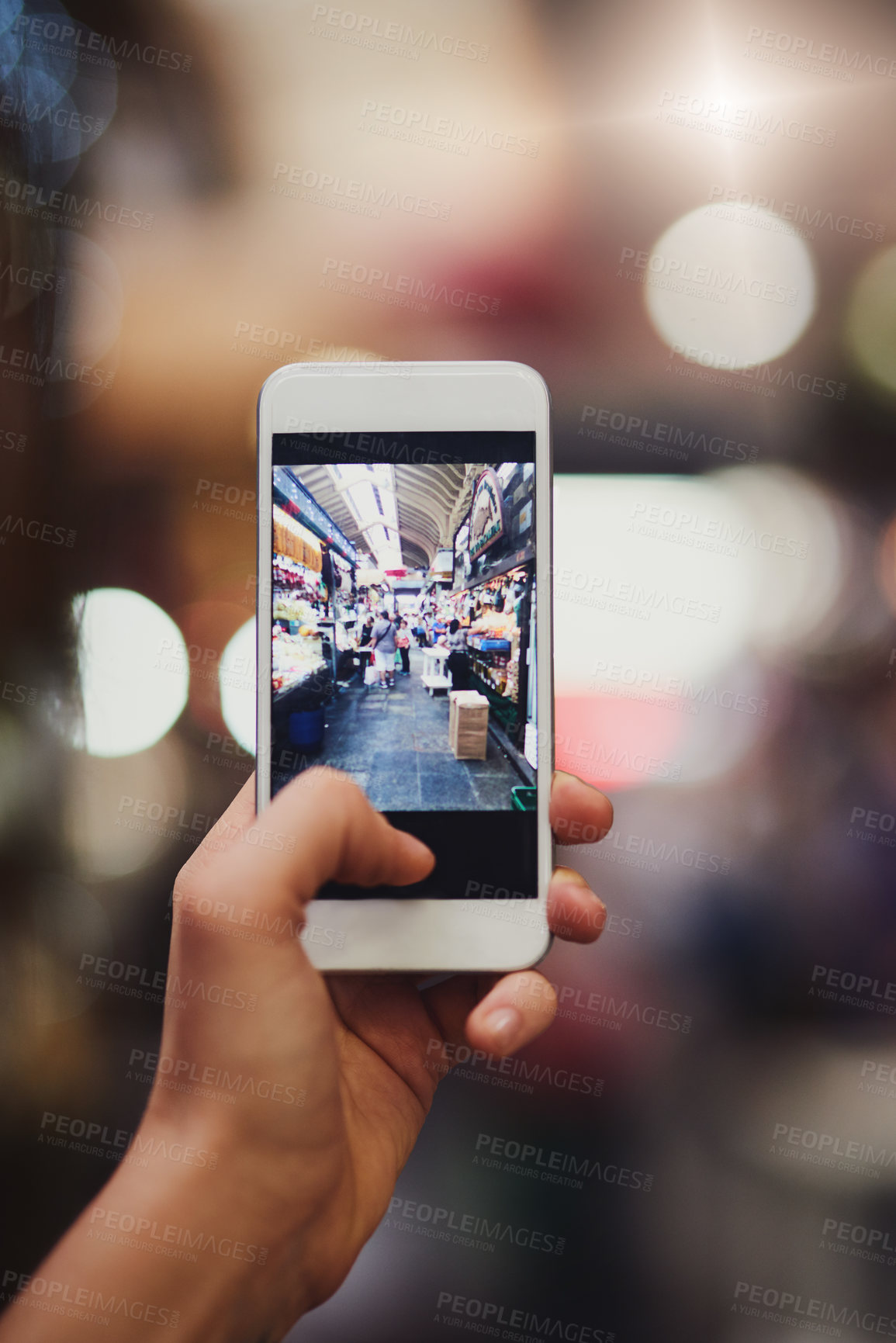 Buy stock photo Shot of an unrecognizable person's hand holding a cellphone and taking photos of a busy market outside during the day