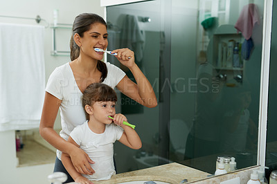 Buy stock photo Shot of a mother and daughter brushing their teeth together in the bathroom at home