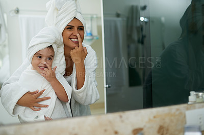 Buy stock photo Shot of a mother and daughter moisturizing their faces together in the bathroom at home