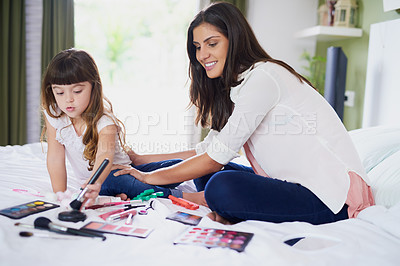 Buy stock photo Shot of a mother and her little daughter playing with makeup on the bed at home
