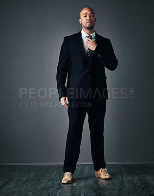 Buy stock photo Studio shot of a handsome young businessman adjusting his tie against a gray background