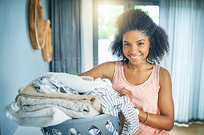 Buy stock photo Portrait of a cheerful young woman  holding a basket of washing while looking at the camera at home during the day