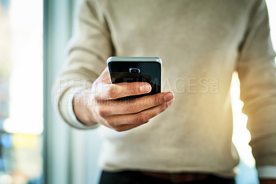 Buy stock photo Closeup shot of an unrecognizable man texting on his phone while standing in the office during the day