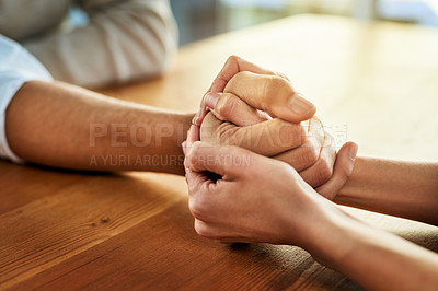 Buy stock photo Cropped shot of two unrecognizable people holding hands while being seated at a table inside during the day