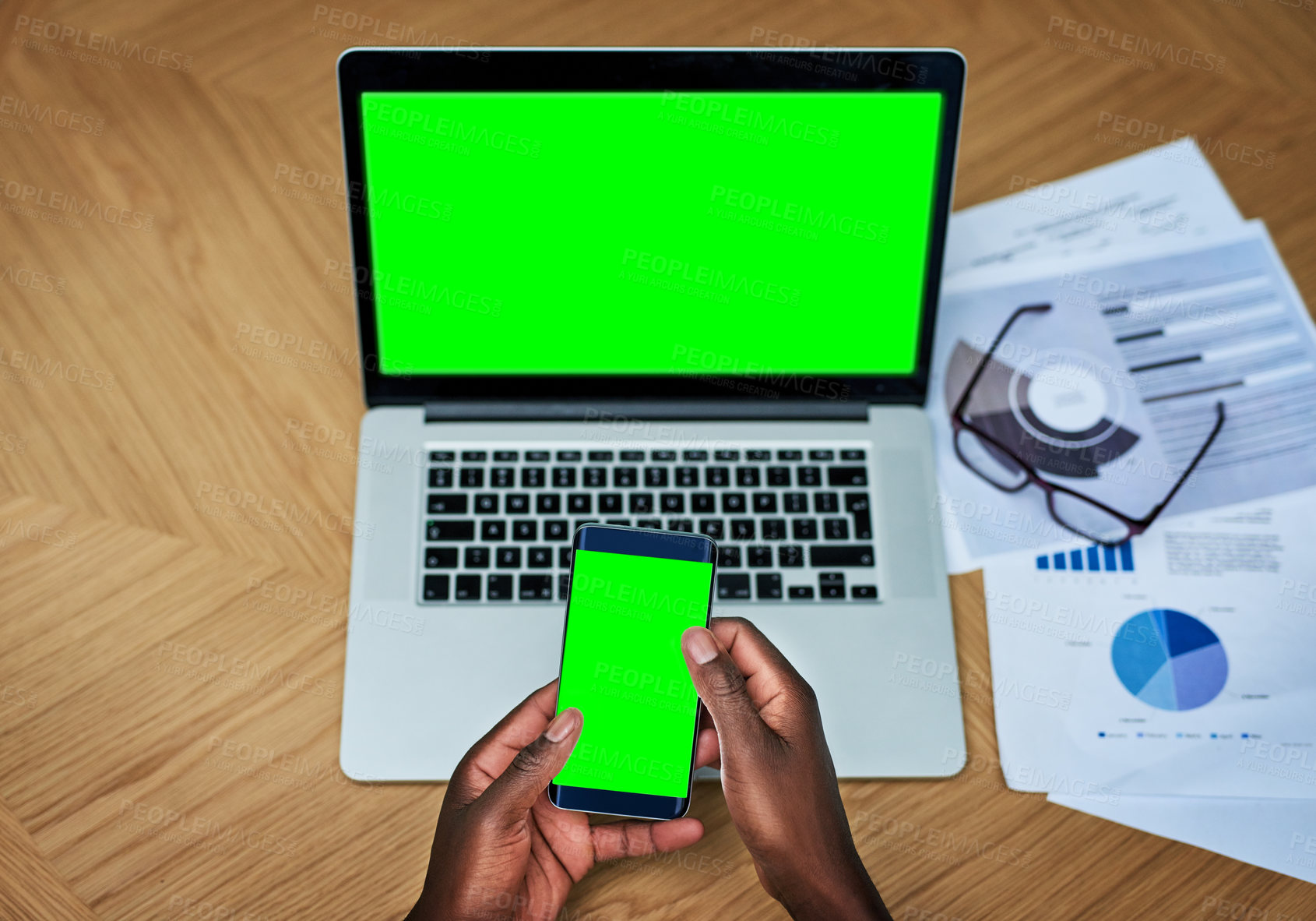 Buy stock photo High angle shot of an unrecognizable businessperson texting on their cellphone while working on a laptop at a desk