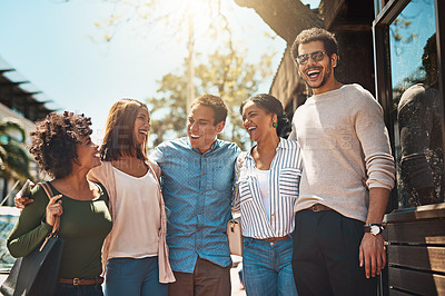Buy stock photo Shot of a cheerful young group of friends walking arm in arm together down a street outside during the day