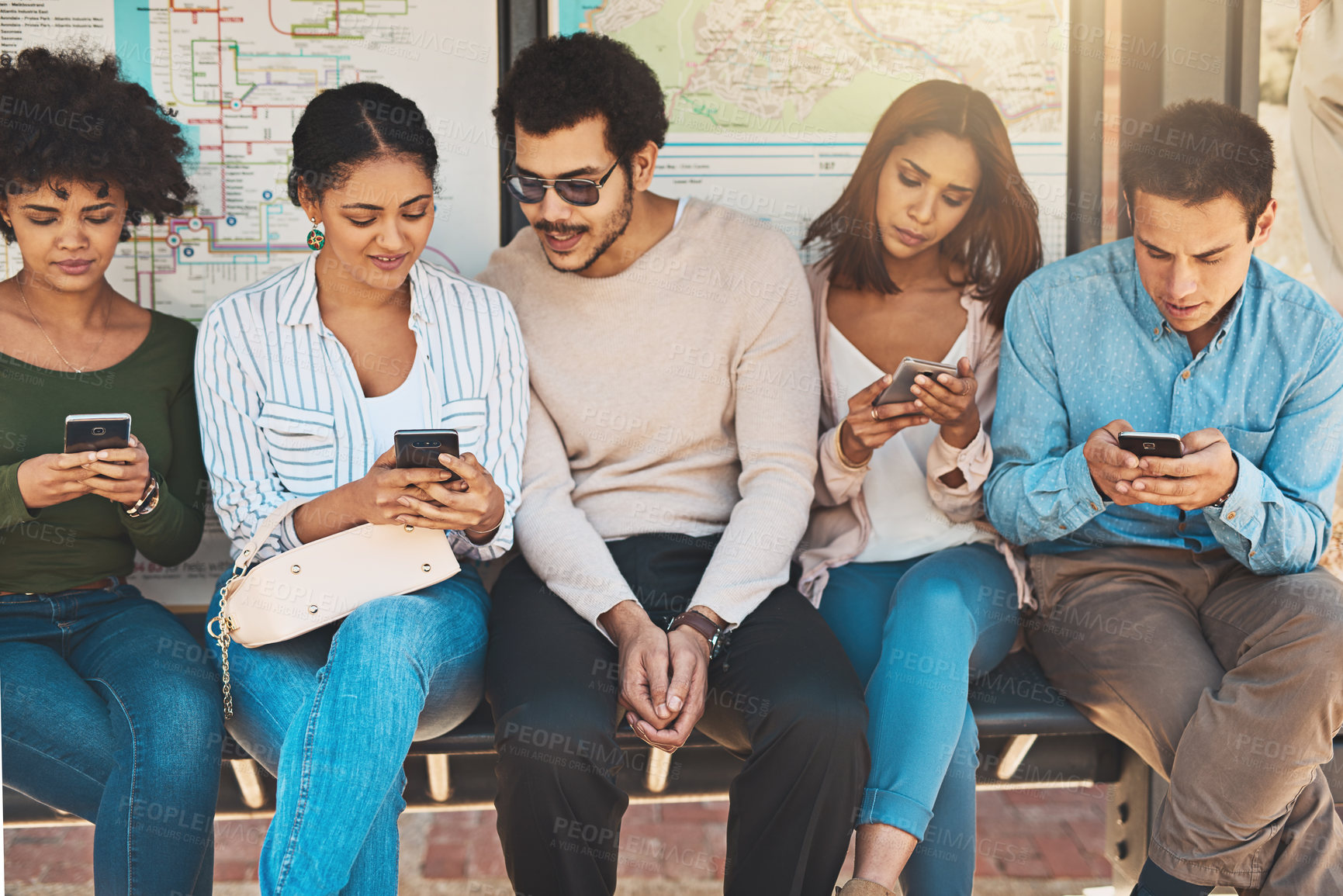 Buy stock photo Shot of a group of focused young friends seated next to each other while texting and browsing on their cellphones outside during the day