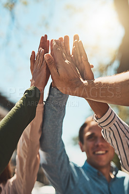 Buy stock photo Shot of a group of cheerful young friends forming a huddle and giving each other a high five outside during the day