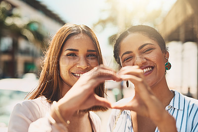 Buy stock photo Portrait of two cheerful young women forming a heart shape with their hands together while standing outside during the day