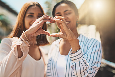 Buy stock photo Shot of two cheerful young women forming a heart shape with their hands together while standing outside during the day