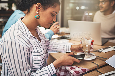 Buy stock photo Shot of a focused young woman texting on her cellphone while being seated at a coffeeshop drinking a hot beverage