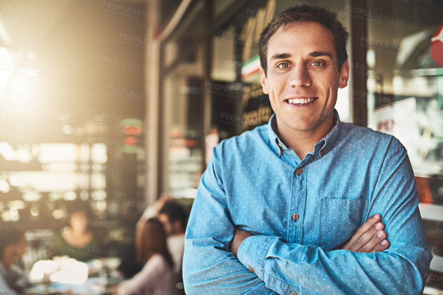 Buy stock photo Portrait of a confident young man standing with his arms folded inside of a coffeeshop during the day