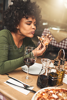 Buy stock photo Shot of a cheerful young woman enjoying a slice of pizza while being seated at a table inside of a restaurant