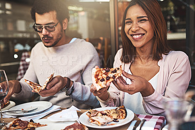 Buy stock photo Shot of a cheerful young woman and man eating pizza together while being seated at a table inside of a restaurant