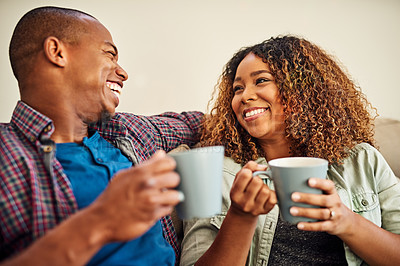 Buy stock photo Shot of a cheerful young couple enjoying a cup of coffee together while being seated on a couch at home during the day
