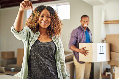 Buy stock photo Portrait of a cheerful young woman holding the keys to her house with her partner in the back carrying boxes