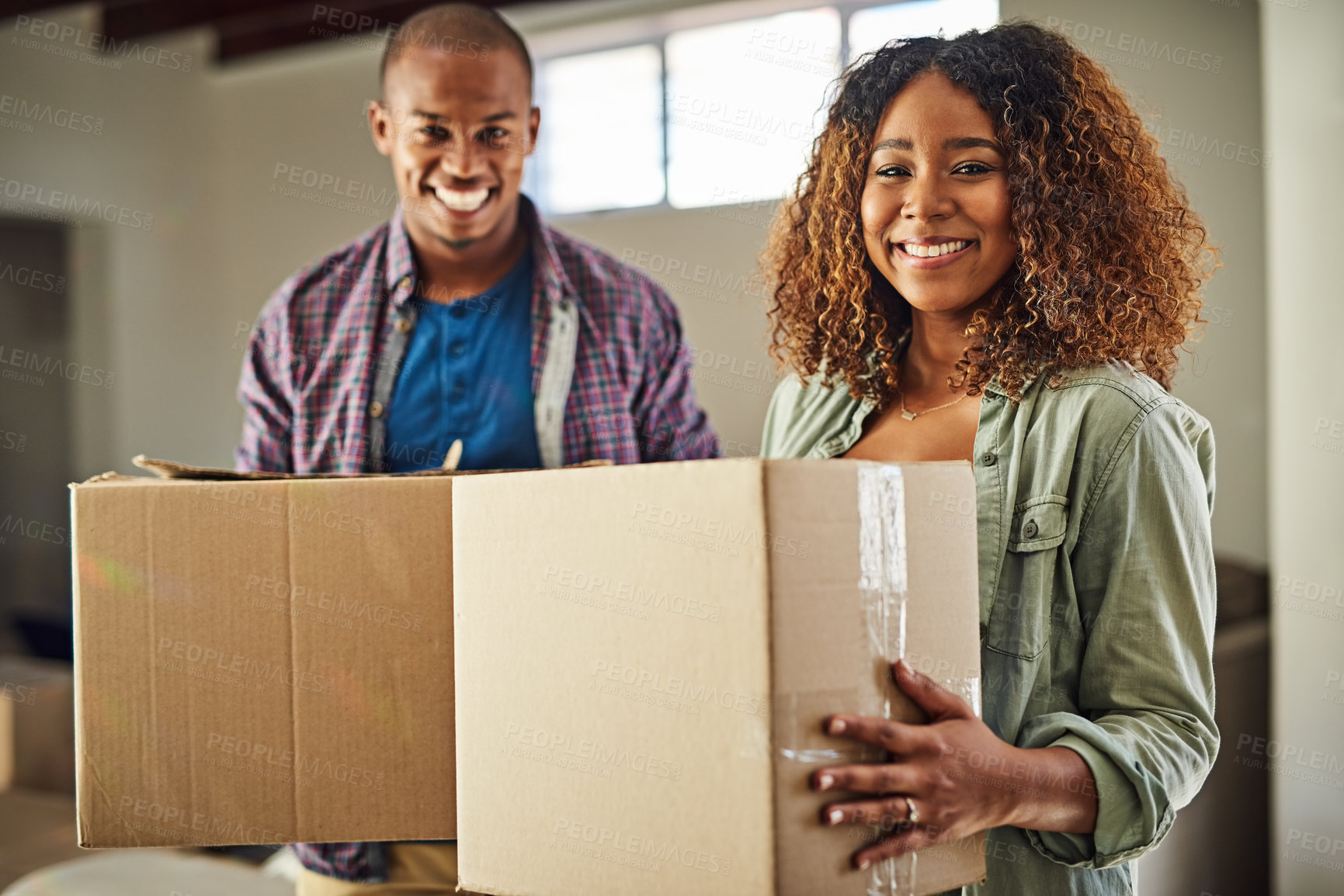 Buy stock photo Portrait of a cheerful young couple carrying boxes together to move into their new home inside during the day