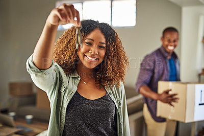 Buy stock photo Portrait of a cheerful young woman holding the keys to her house with her partner in the back carrying boxes