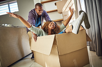 Buy stock photo Shot of a cheerful young woman inside of a box with her partner pushing the box inside at home during the day