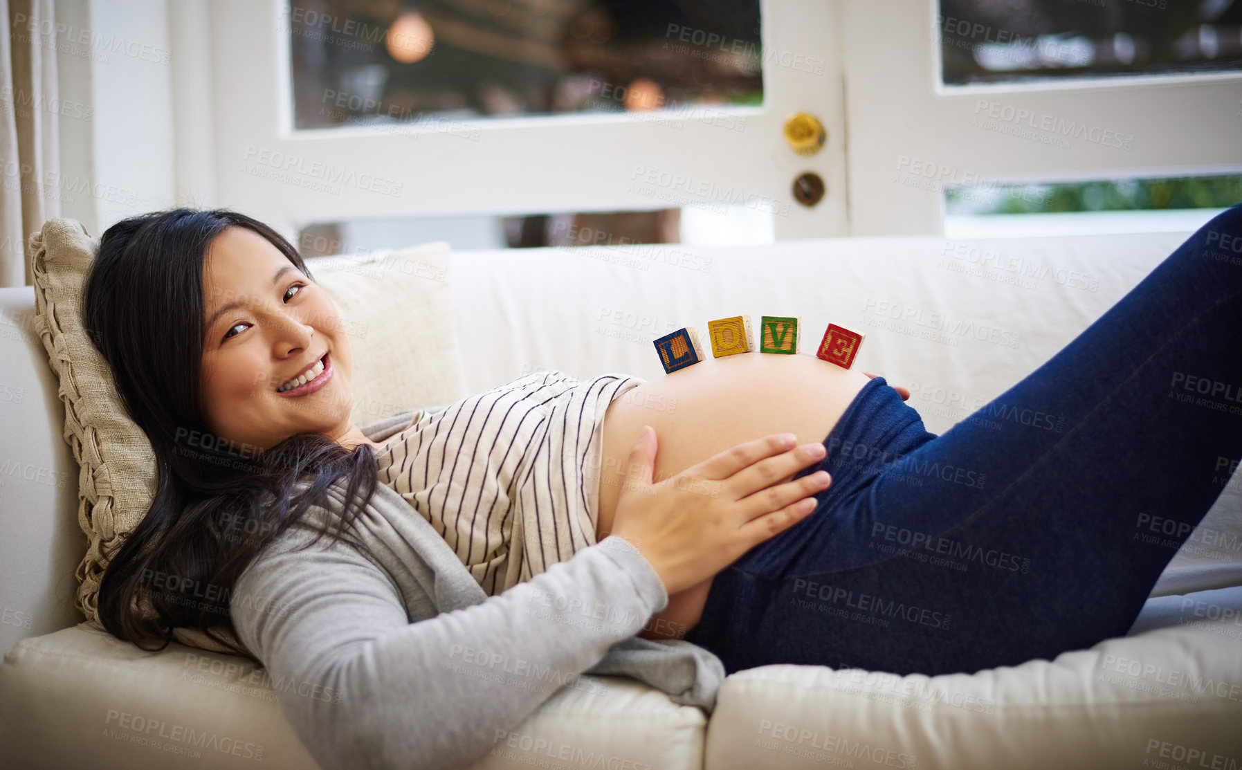 Buy stock photo Portrait of an attractive young pregnant woman balancing wooden blocks on her tummy while relaxing on the sofa at home