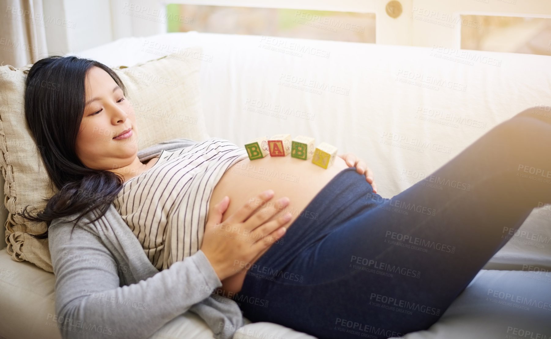 Buy stock photo Shot of an attractive young pregnant woman balancing wooden blocks on her tummy while relaxing on the sofa at home