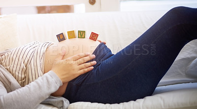 Buy stock photo Shot of an unrecognizable young pregnant woman balancing wooden blocks on her tummy while relaxing on the sofa at home