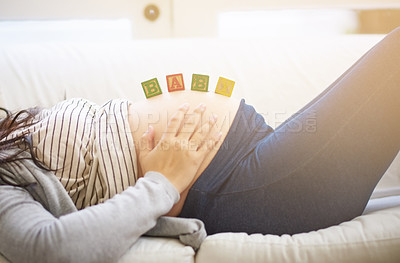 Buy stock photo Shot of an unrecognizable young pregnant woman balancing wooden blocks on her tummy while relaxing on the sofa at home