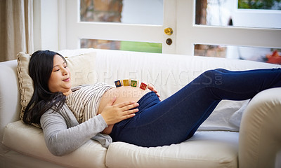 Buy stock photo Shot of an attractive young pregnant woman balancing wooden blocks on her tummy while relaxing on the sofa at home