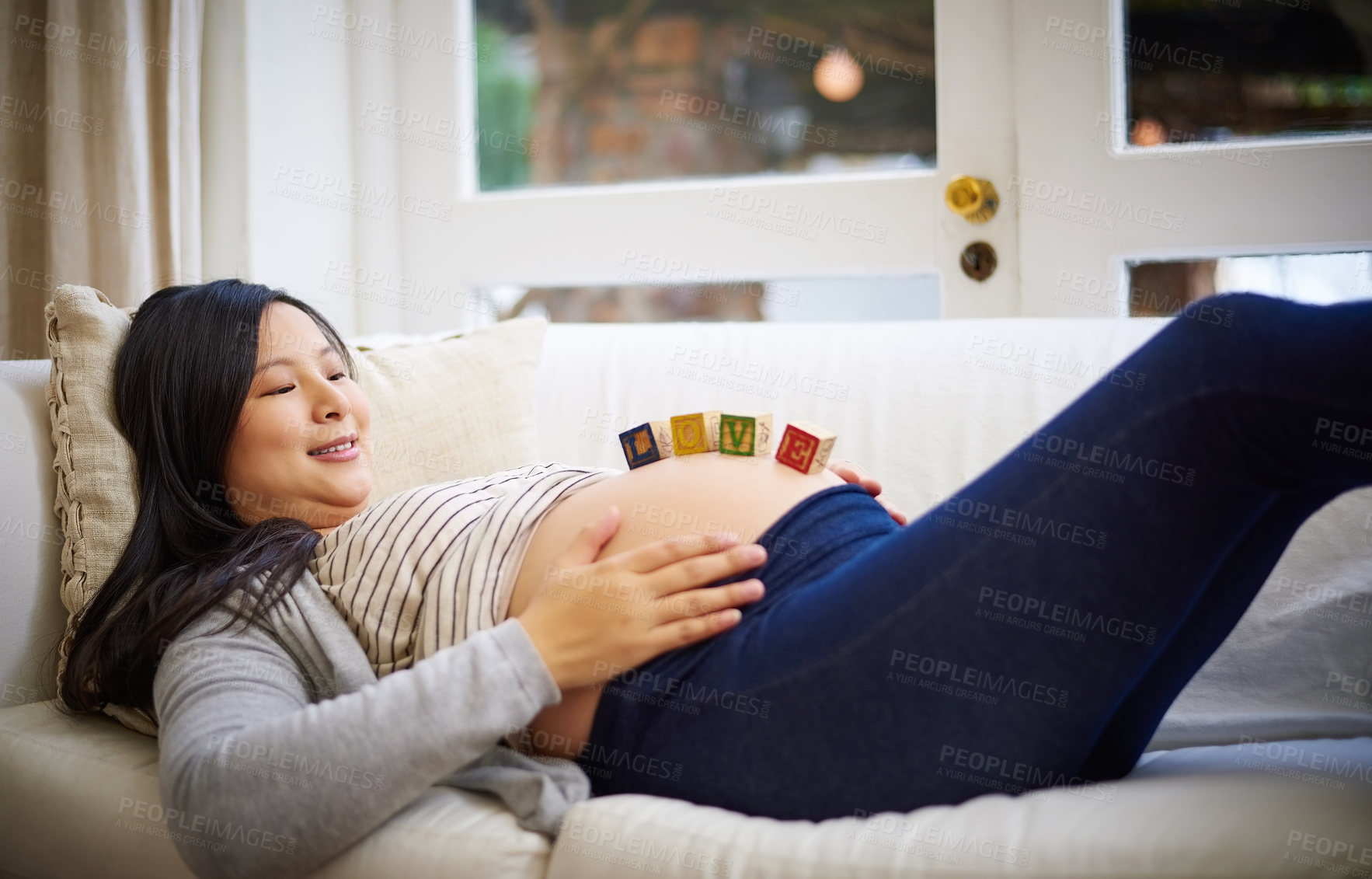 Buy stock photo Shot of an attractive young pregnant woman balancing wooden blocks on her tummy while relaxing on the sofa at home