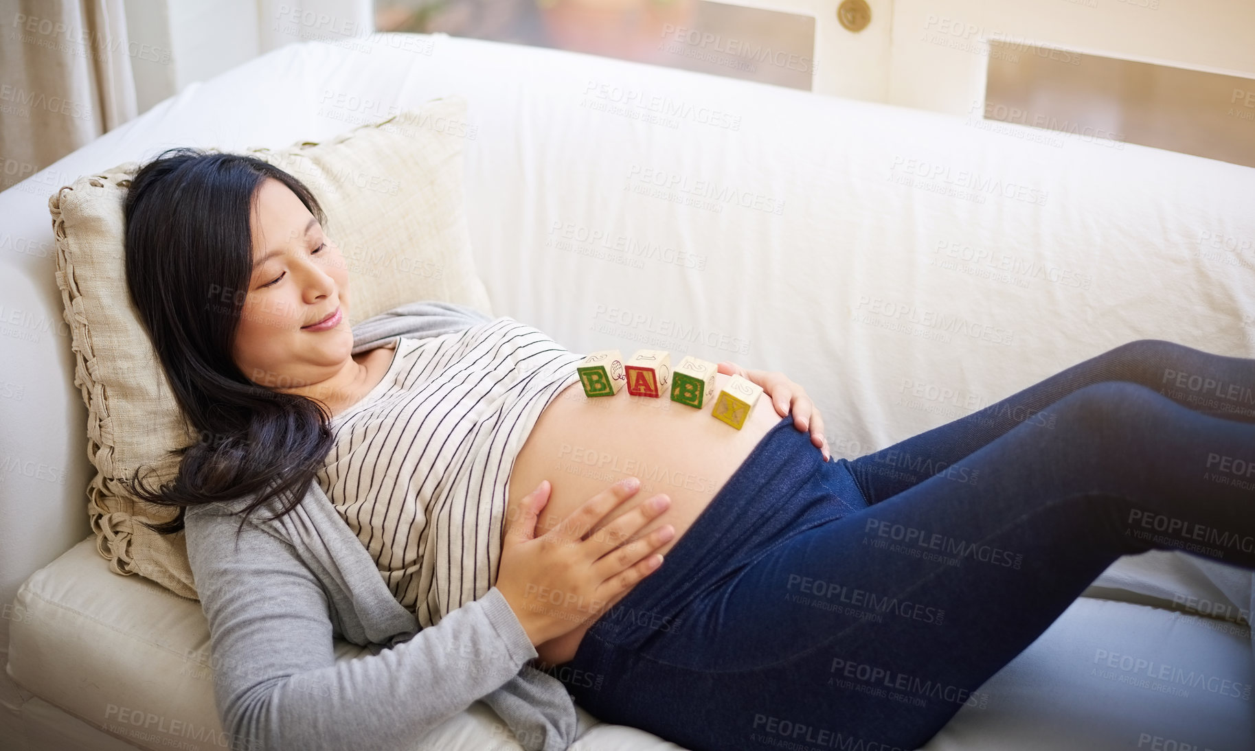 Buy stock photo Shot of an attractive young pregnant woman balancing wooden blocks on her tummy while relaxing on the sofa at home