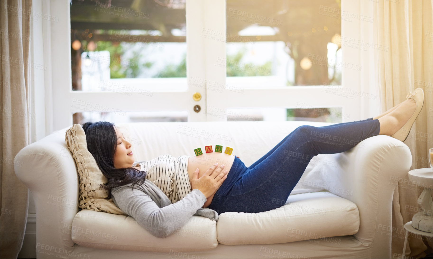 Buy stock photo Shot of an attractive young pregnant woman balancing wooden blocks on her tummy while relaxing on the sofa at home