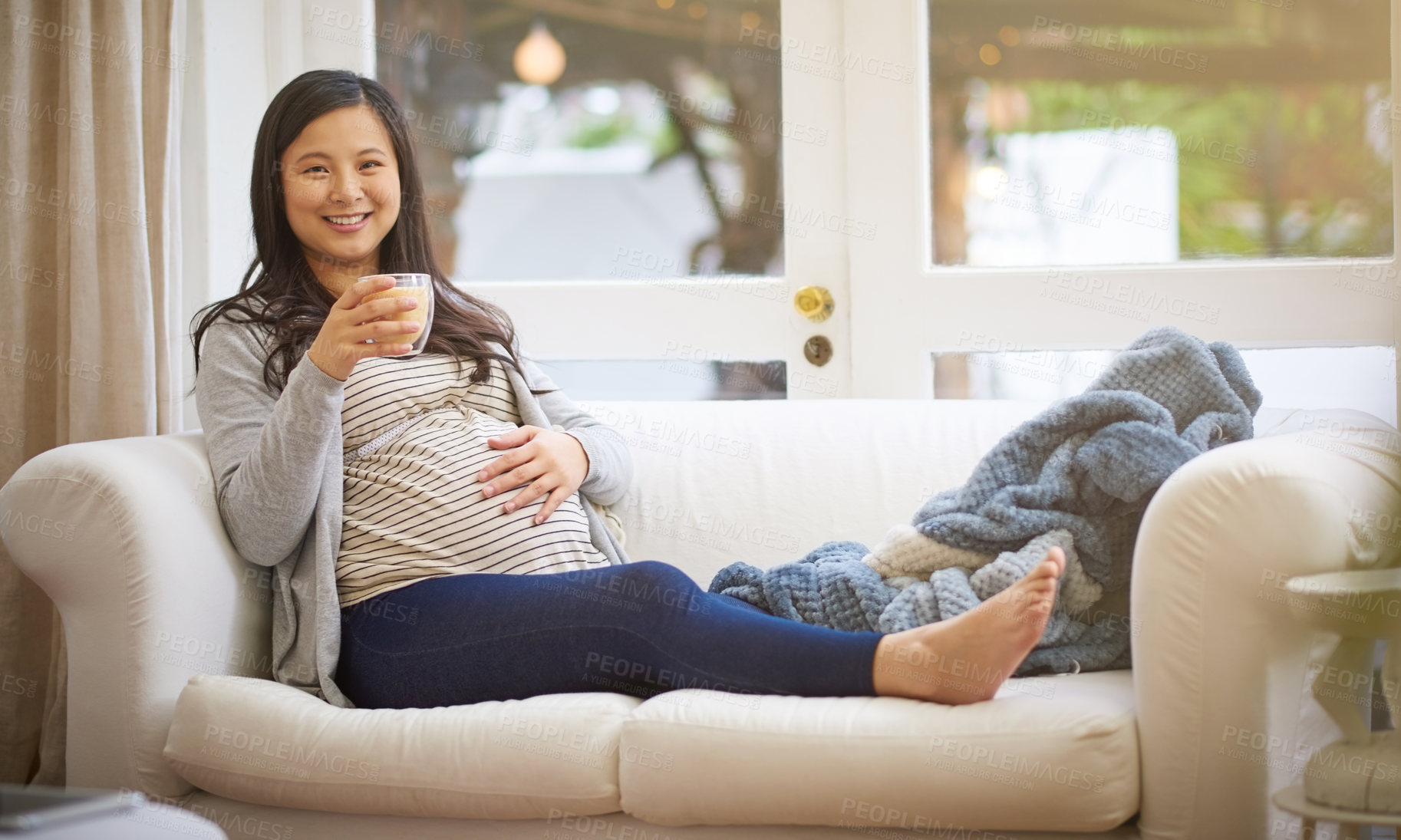 Buy stock photo Portrait of an attractive young pregnant woman drinking an iced coffee while relaxing on the sofa at home