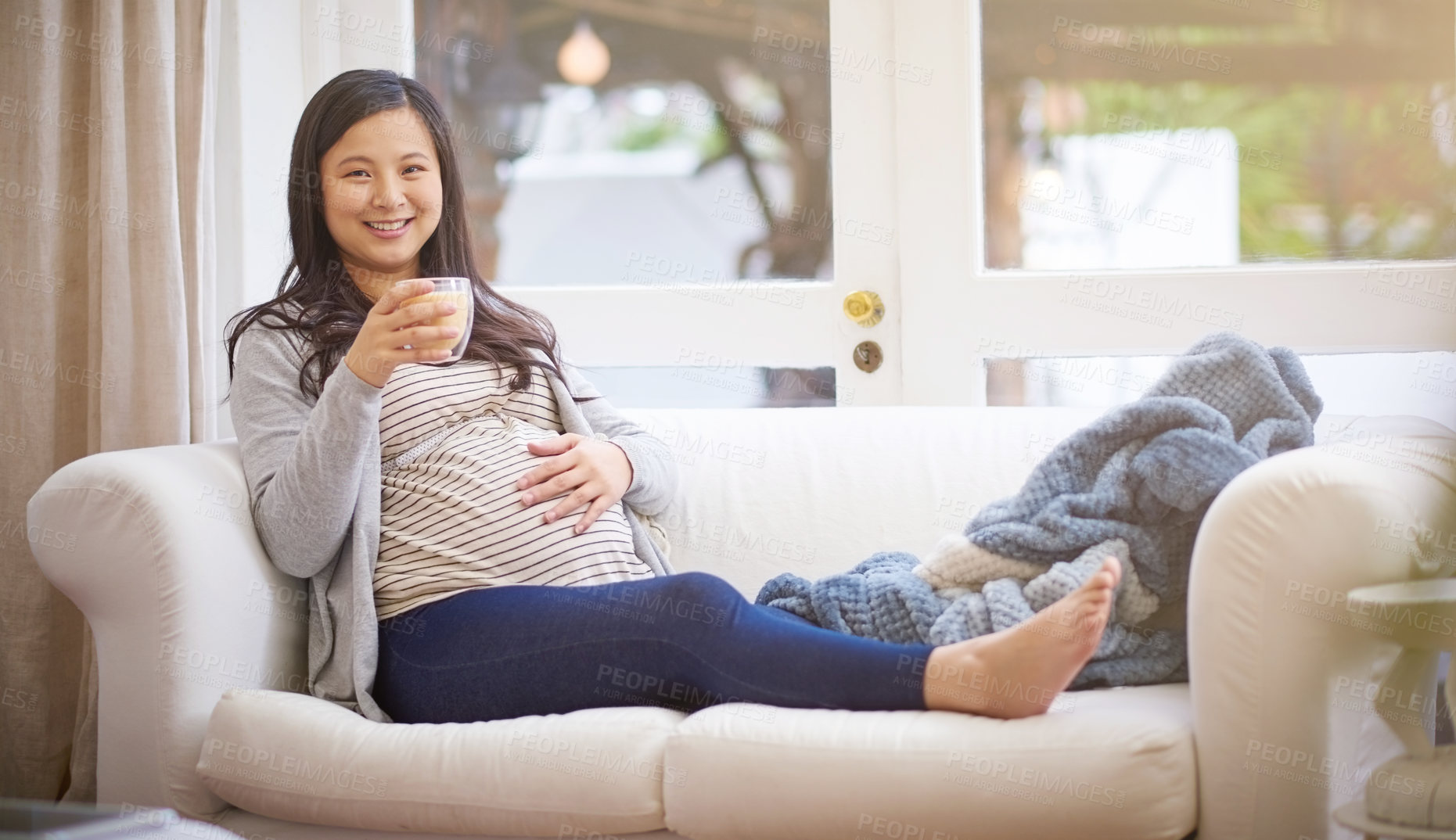 Buy stock photo Portrait of an attractive young pregnant woman drinking an iced coffee while relaxing on the sofa at home