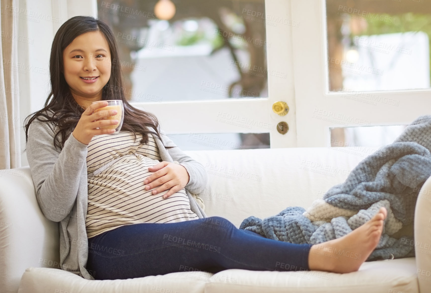 Buy stock photo Portrait of an attractive young pregnant woman drinking an iced coffee while relaxing on the sofa at home