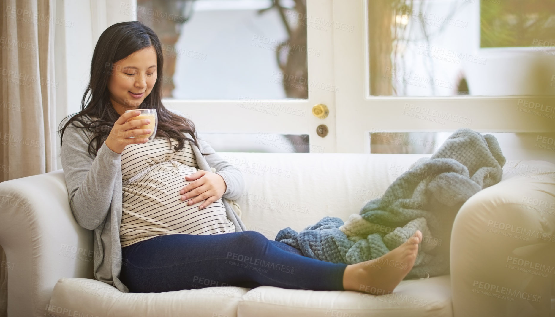 Buy stock photo Shot of an attractive young pregnant woman drinking an iced coffee while relaxing on the sofa at home