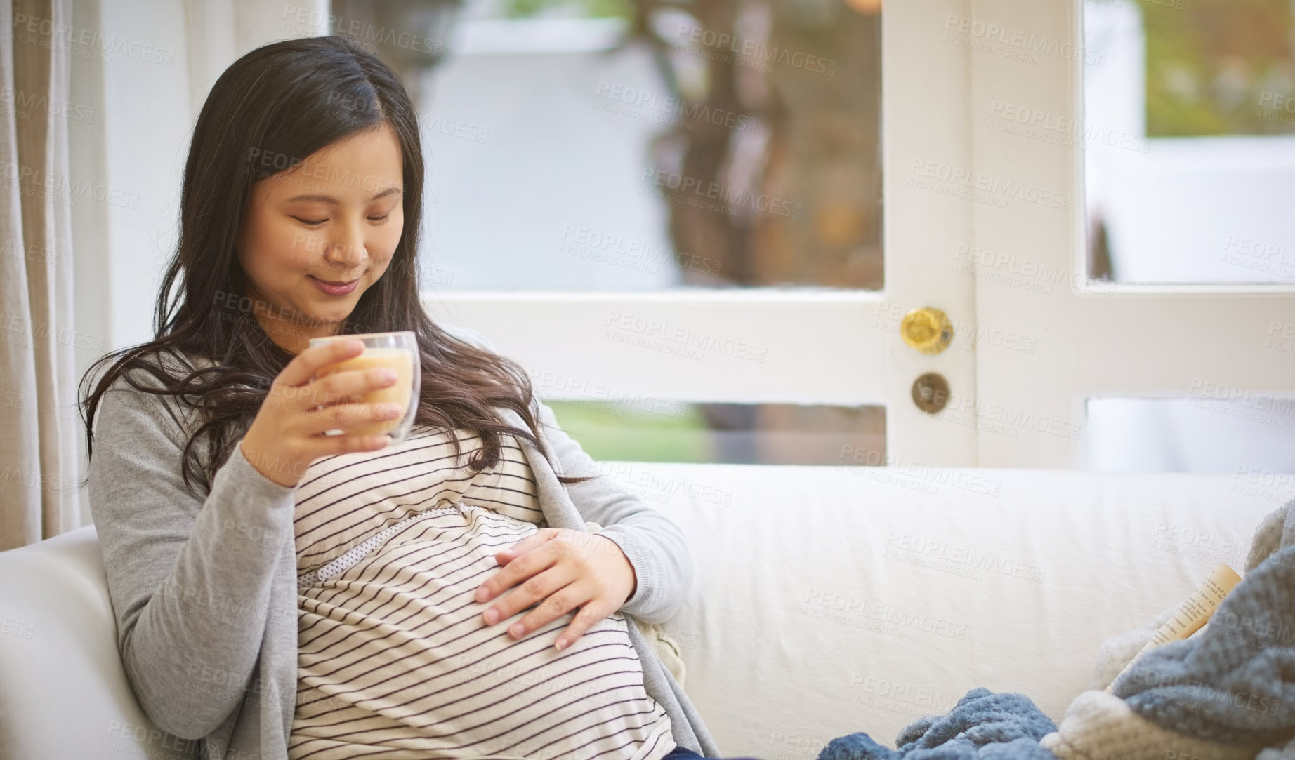 Buy stock photo Shot of an attractive young pregnant woman drinking an iced coffee while relaxing on the sofa at home