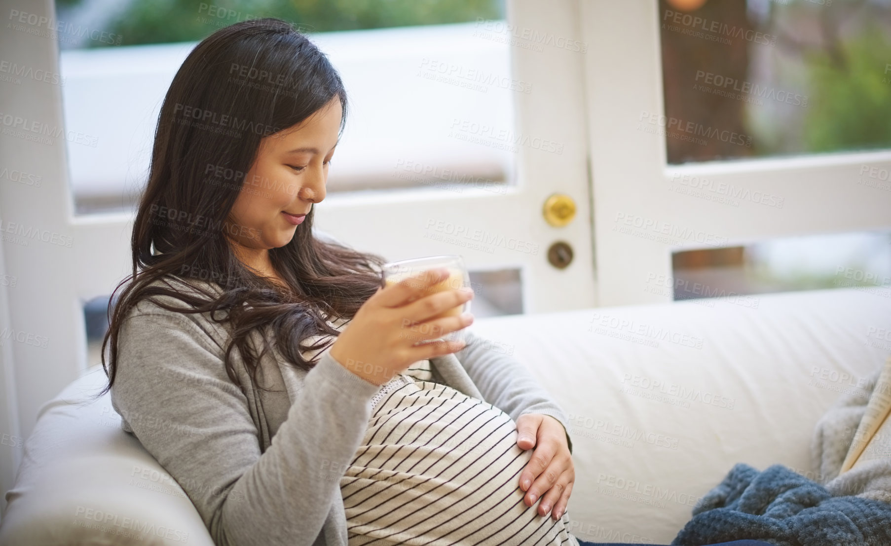 Buy stock photo Shot of an attractive young pregnant woman drinking an iced coffee while relaxing on the sofa at home