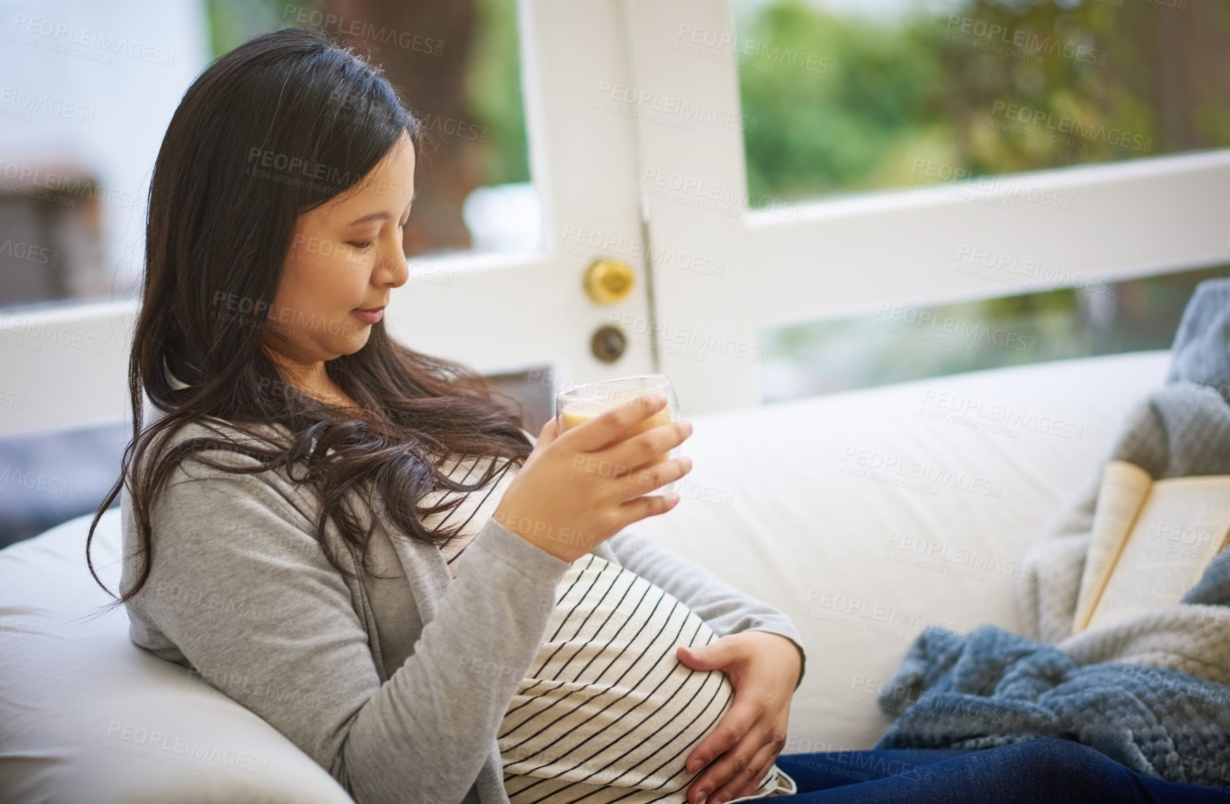 Buy stock photo Shot of an attractive young pregnant woman drinking an iced coffee while relaxing on the sofa at home