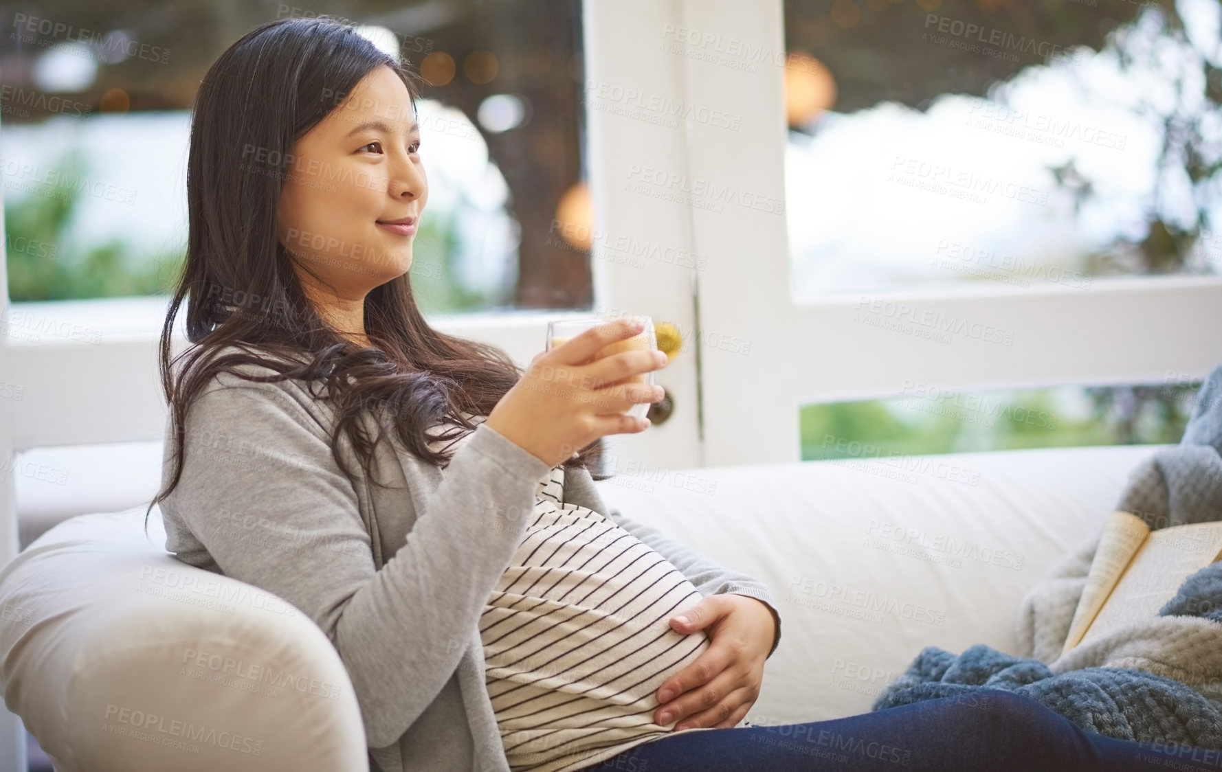 Buy stock photo Shot of an attractive young pregnant woman drinking an iced coffee while relaxing on the sofa at home