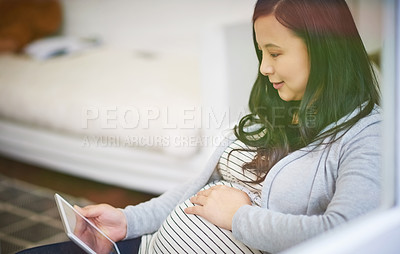 Buy stock photo Shot of an attractive young pregnant woman using her tablet while relaxing on the sofa at home